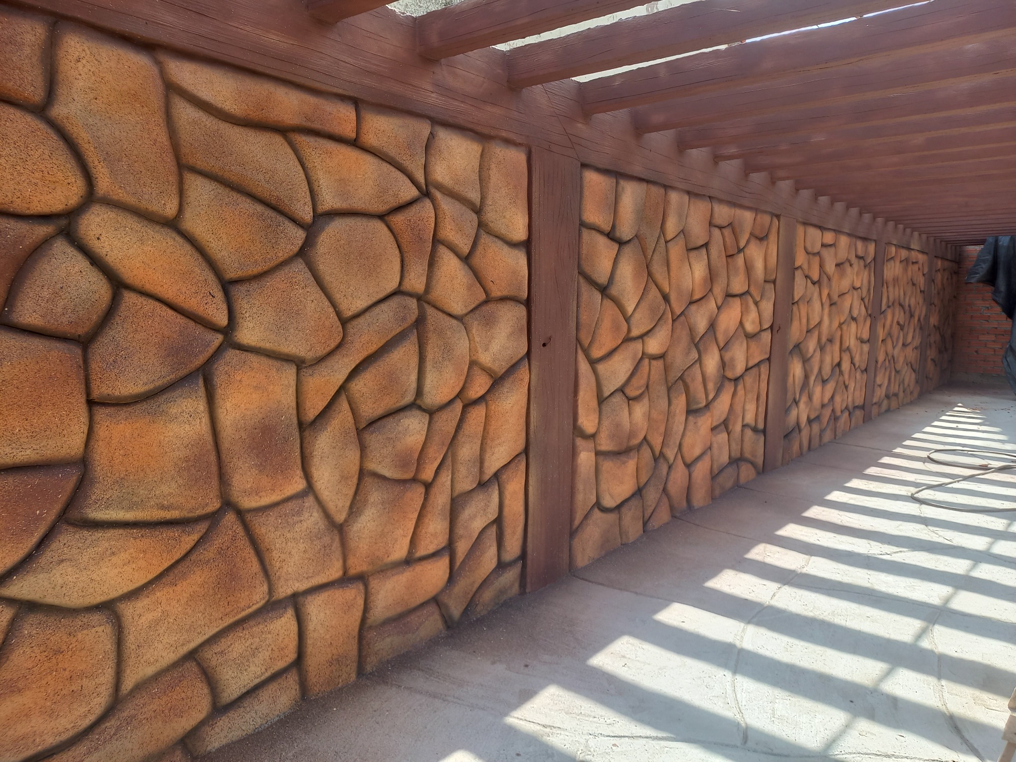 Pergola project with a stone-inspired wall and some wood forms recreated by Gisa Matos in cement